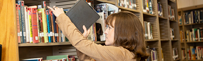 A person pulling a book from a library shelf